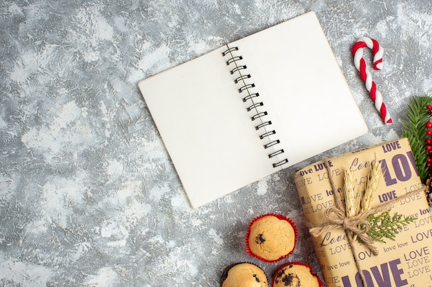 Vista anterior del cuaderno abierto y hermoso regalo de Navidad con inscripción de amor, pequeños cupcakes y accesorios de decoración de ramas de abeto, cono de coníferas en la superficie del hielo