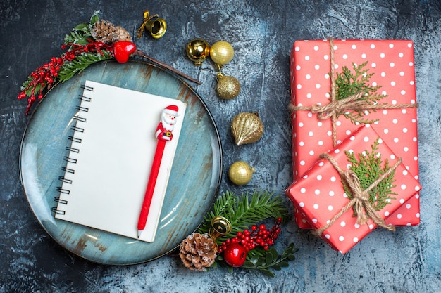 Vista anterior del cuaderno con bolígrafo sobre placa azul, accesorios decorativos y una caja de regalo sobre fondo oscuro