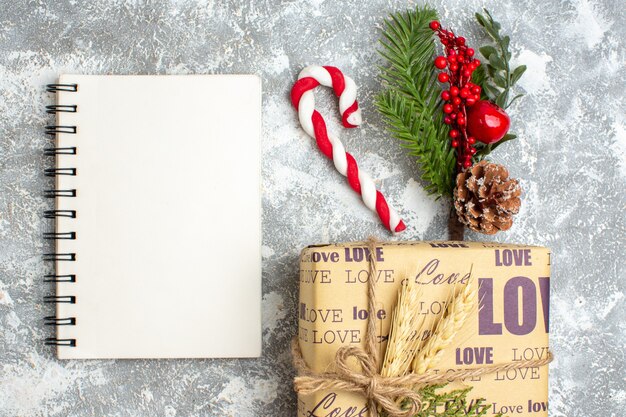 Vista anterior del cuaderno cerrado y hermoso regalo lleno de Navidad con inscripción de amor pequeños cupcakes cand ramas de abeto accesorios de decoración cono de coníferas en superficie de hielo