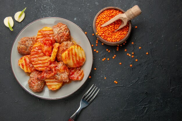 Vista anterior de la deliciosa cena con patatas y carne, tomate, ajo, tenedor, lentejas en negro