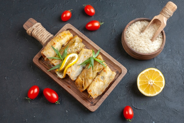 Vista anterior de la deliciosa comida de dolma en una tabla de cortar de madera servida con tomate verde limón y arroz en la pared oscura