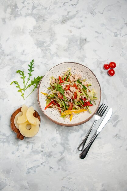 Vista anterior de la deliciosa ensalada de pollo con verduras, tomates, piñas secas, cubiertos en superficie blanca manchada con espacio libre