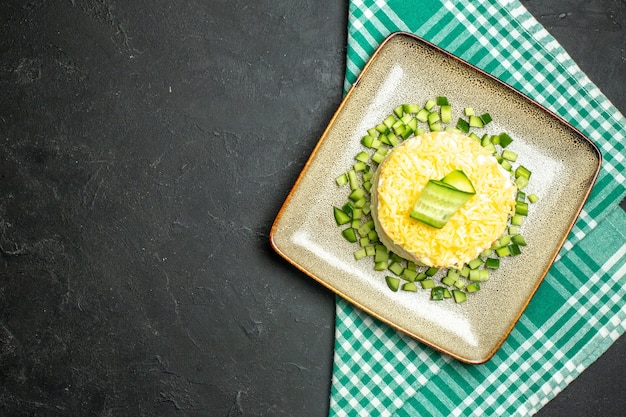 Vista anterior de una deliciosa ensalada servida con pepino picado en la mitad de la toalla doblada verde despojado sobre fondo oscuro