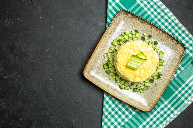 Vista anterior de una deliciosa ensalada servida con pepino picado en la mitad de la toalla doblada verde despojado sobre fondo oscuro