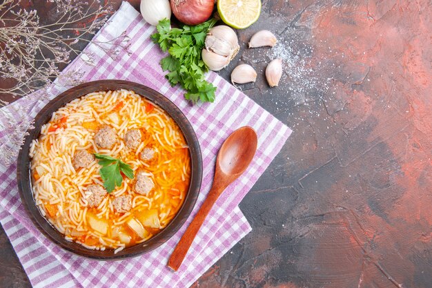 Vista anterior de una deliciosa sopa de pollo con fideos verdes y una cuchara en una toalla despojada rosa botella de aceite ajo limón sobre fondo oscuro