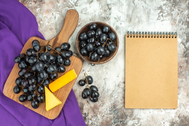 Vista anterior del delicioso racimo de uva negra fresca y queso sobre tabla de cortar de madera
