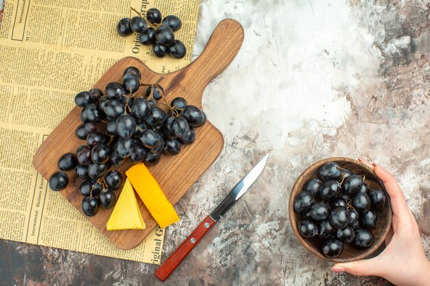 Vista anterior del delicioso racimo de uva negra fresca y varios tipos de queso en la tabla de cortar de madera