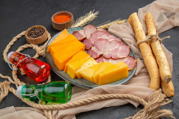 Vista anterior de deliciosos bocadillos botellas caídas pimientos sobre una toalla y cuerda sobre un fondo negro