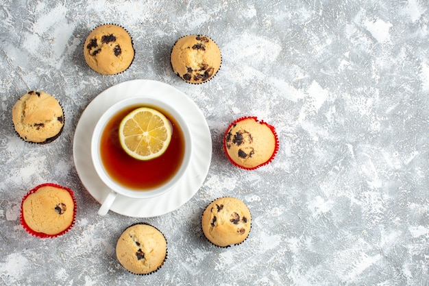 Vista anterior de deliciosos cupcakes pequeños con chocolate alrededor de una taza de té negro en el lado derecho sobre la superficie del hielo