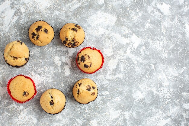 Vista anterior de deliciosos cupcakes pequeños con chocolate en el lado derecho sobre la superficie del hielo