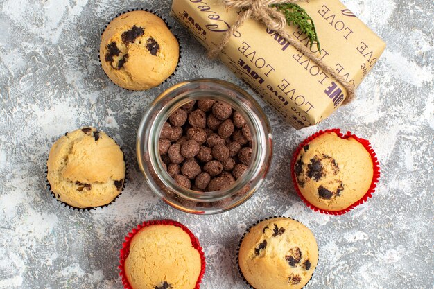 Vista anterior de deliciosos cupcakes pequeños y chocolate en una olla de vidrio junto al regalo de Navidad sobre la superficie del hielo