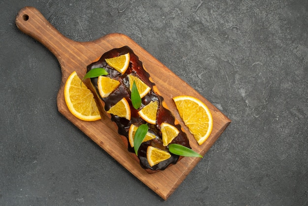 Vista anterior de deliciosos pasteles decorados con naranja y chocolate en la tabla de cortar en el cuadro negro