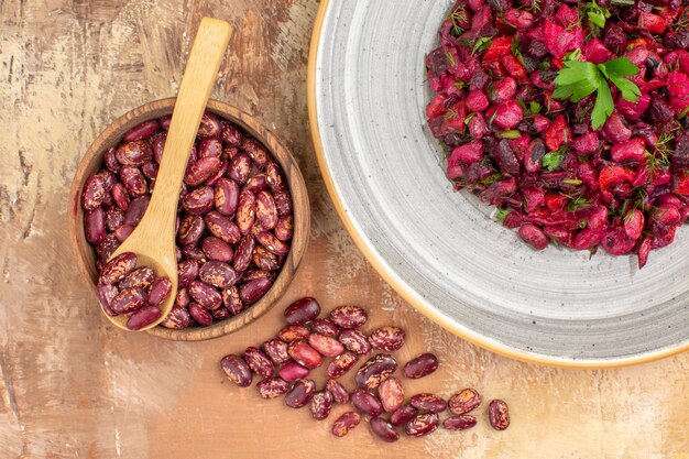 Vista anterior de ensalada con frijoles en vinagre dentro y fuera de la olla marrón con cuchara sobre fondo de colores mezclados