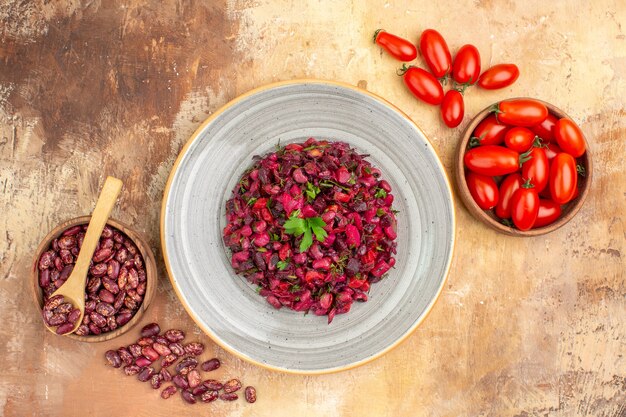 Vista anterior de la ensalada vinegred con frijoles dentro y fuera de la olla marrón con cuchara y tomates sobre fondo de colores mezclados