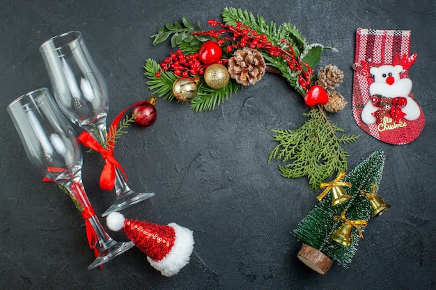 Vista anterior del estado de ánimo navideño con copas de cristal caído ramas de abeto calcetín de árbol de Navidad sombrero de santa claus sobre fondo oscuro