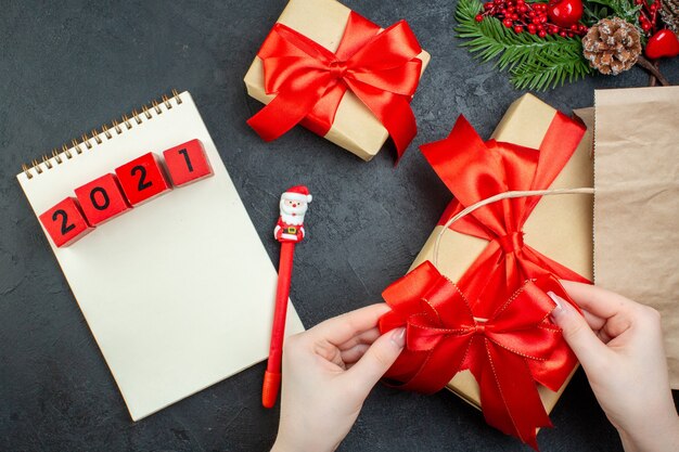 Vista anterior del estado de ánimo navideño con hermosos regalos con cinta roja y números en el cuaderno con lápiz sobre la mesa oscura