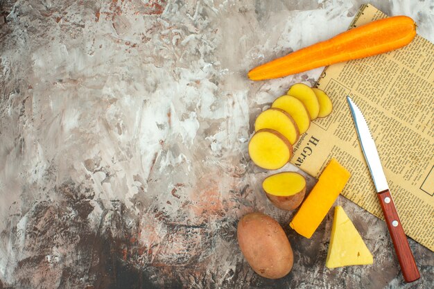 Vista anterior de fondo de cocción con diversas verduras y dos tipos de cuchillo de queso en un periódico viejo sobre fondo de color mixto