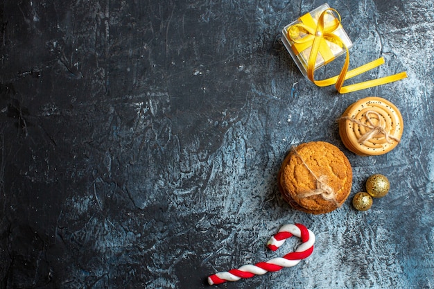 Vista anterior del fondo de Navidad con caja de regalo amarilla y accesorios de decoración de dulces de galletas sobre fondo oscuro