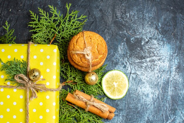 Vista anterior del fondo de Navidad con hermosas cajas de regalo amarillas y galletas apiladas limón canela limas en el lado derecho de la mesa oscura