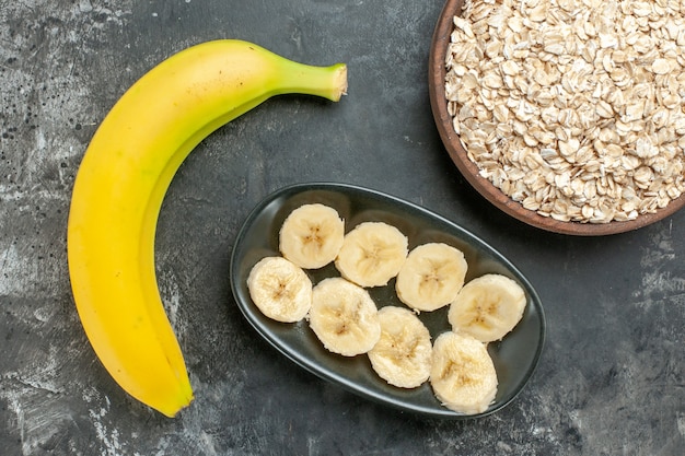 Vista anterior de la fuente de nutrición orgánica plátano fresco picado y salvado de avena y entero en una olla marrón sobre fondo oscuro