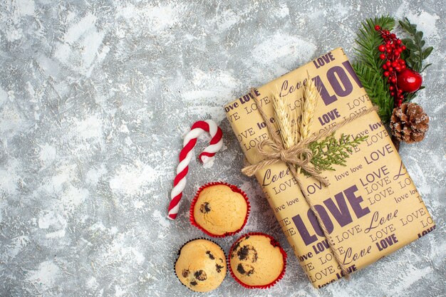 Vista anterior del hermoso regalo de Navidad con inscripción de amor y pequeños cupcakes accesorios de decoración de ramas de abeto cono de coníferas en la superficie del hielo