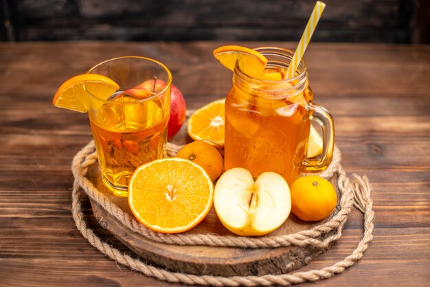 Vista anterior de jugo orgánico fresco en una botella y vaso servido con tubo y frutas sobre una tabla para cortar