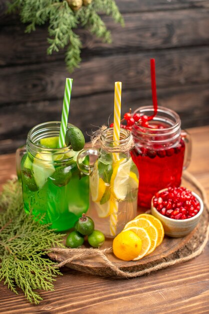 Vista anterior de jugos orgánicos frescos en botellas servidos con tubos y frutas sobre una tabla de cortar de madera