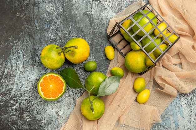 Vista anterior de kumquats frescos y limones en una canasta negra sobre una toalla y cuatro limones en imágenes de fondo gris