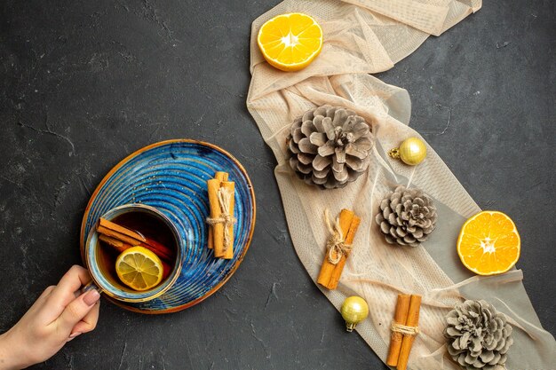 Vista anterior de limas canela cortadas naranjas y tres conos de coníferas en una toalla de color nude una taza de té negro sobre fondo de color negro