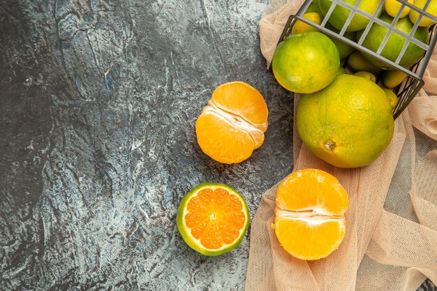 Vista anterior de limones frescos en una canasta negra caída sobre una toalla en imágenes de mesa gris