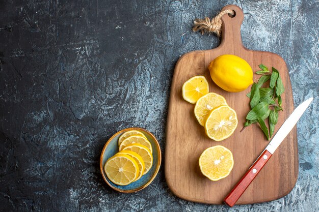 Vista anterior de limones frescos y cuchillo de menta sobre una tabla de cortar de madera en el lado izquierdo sobre fondo oscuro