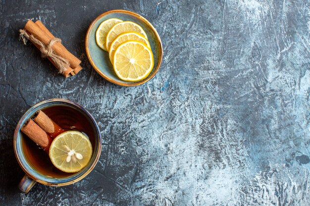 Vista anterior de limones frescos y una taza de té negro con canela en el lado derecho sobre fondo oscuro