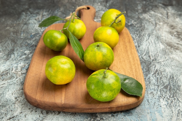 Foto gratuita vista anterior de mandarinas verdes frescas con hojas sobre tabla de cortar de madera sobre fondo gris