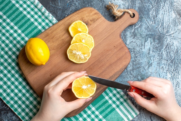 Vista anterior de una mano para picar limones frescos sobre una tabla de cortar de madera sobre fondo oscuro