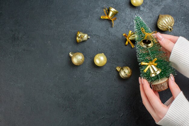 Vista anterior de la mano que sostiene el árbol de navidad y accesorios de decoración sobre fondo oscuro