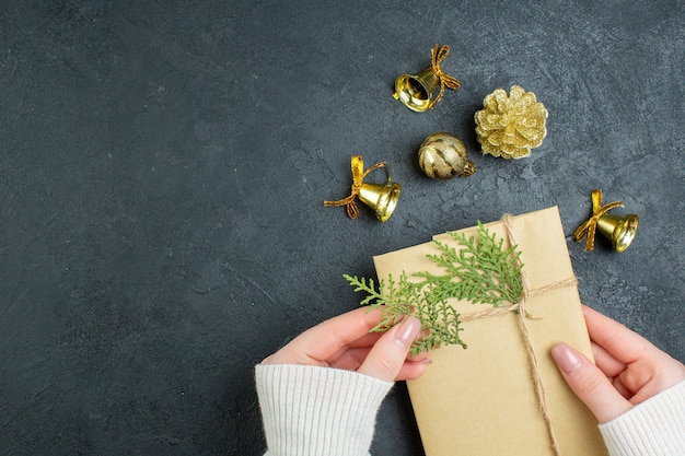 Vista anterior de la mano que sostiene la caja de regalo y accesorios de decoración sobre fondo oscuro