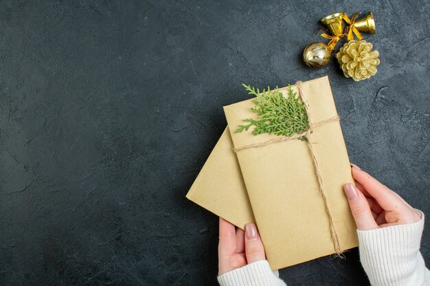 Vista anterior de la mano que sostiene cajas de regalo y accesorios de decoración sobre fondo oscuro