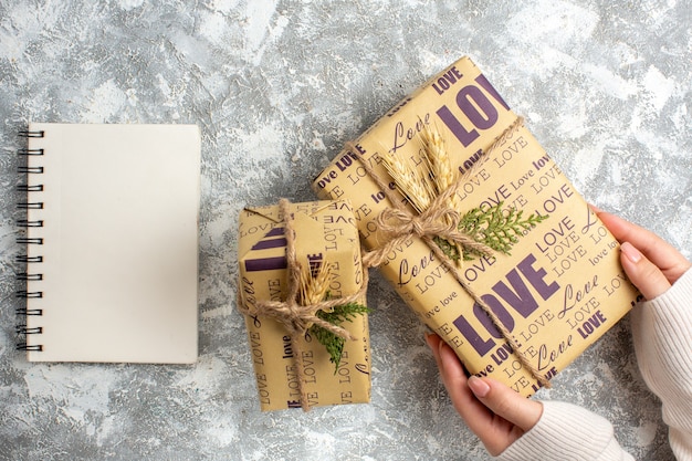 Vista anterior de la mano que sostiene un hermoso regalo para Navidad y un cuaderno cerrado sobre la superficie del hielo