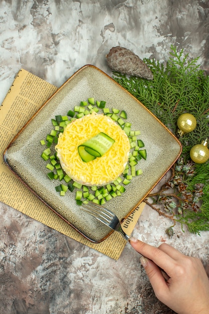 Vista anterior de la mano que sostiene el tenedor en una sabrosa ensalada servida con pepino picado y un tenedor de cuchillo en un periódico viejo