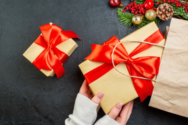 Vista anterior de la mano sacando una hermosa caja de regalo de una bolsa sobre fondo negro