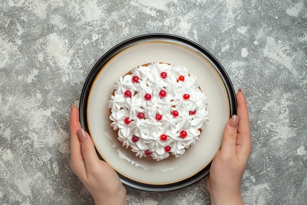 Vista anterior de la mano sosteniendo un plato con un delicioso pastel cremoso decorado con frutas sobre fondo de hielo