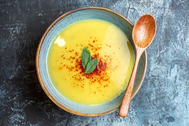 Vista anterior de una olla azul con una sabrosa sopa servida con menta y una cuchara de madera en el cuadro azul