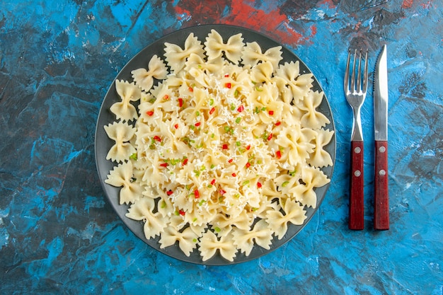 Foto gratuita vista anterior de pasta farfalle italiana cruda con verduras y cubiertos sobre fondo azul.