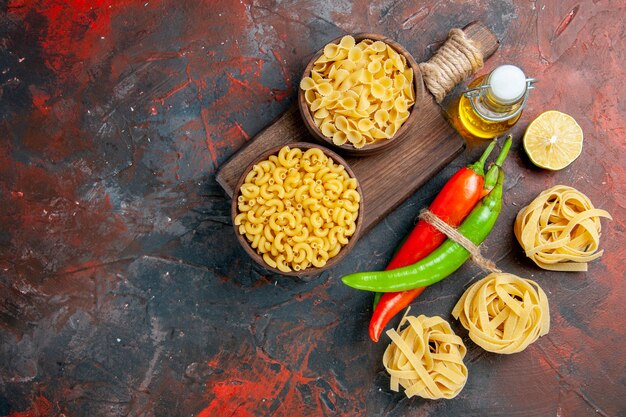 Vista anterior de pastas crudas pimientos de cayena atados entre sí con una botella de aceite de cuerda ajo limón sobre tabla de colores mezclados