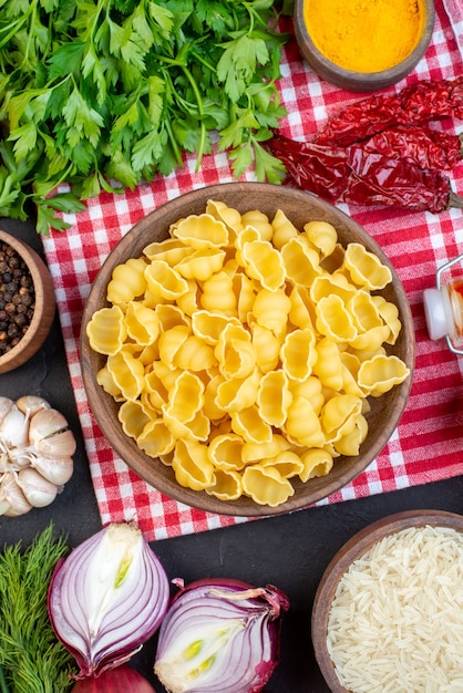 Foto gratuita vista anterior de pastas crudas sobre una toalla despojada de rojo jengibre amarillo arroz con pimiento seco un paquete verde en el cuadro negro