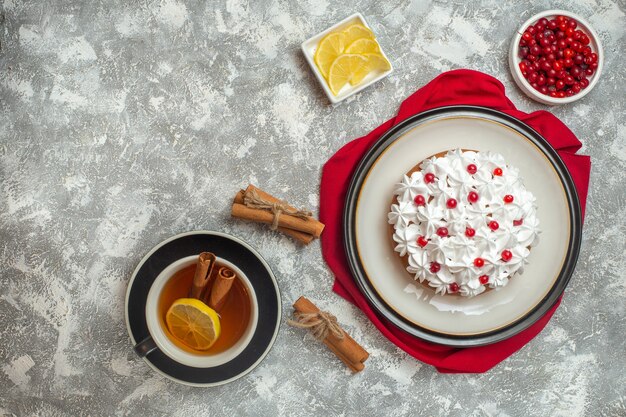 Vista anterior de pastel cremoso decorado con frutas sobre una toalla roja y una taza de té negro con limones canela