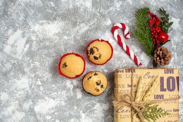 Vista anterior de pequeños cupcakes hermoso regalo lleno de Navidad con inscripción de amor y accesorios de decoración de ramas de abeto cono de coníferas en el lado izquierdo sobre la superficie del hielo