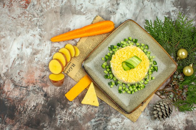 Vista anterior de sabrosa ensalada en un periódico antiguo y dos tipos de queso y zanahorias, patatas picadas, accesorios de año nuevo en la tabla de colores mezclados