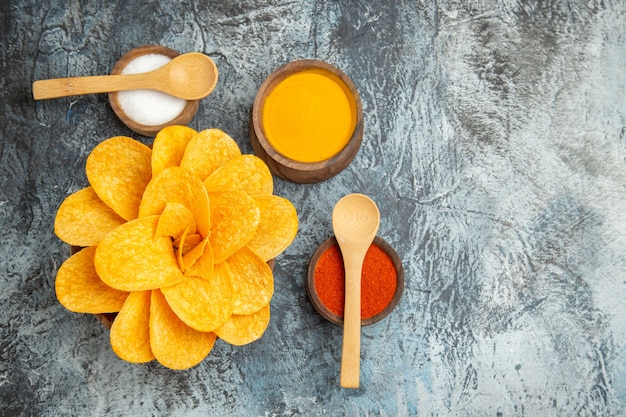 Vista anterior de sabrosas papas fritas decoradas como diferentes especias en forma de flor con cucharas y cuaderno sobre mesa gris