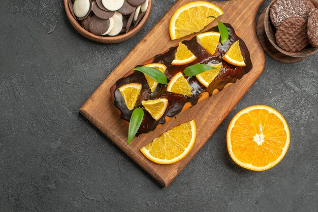 Vista anterior de sabrosos pasteles cortan limones con galletas en la tabla de cortar en bakground oscuro